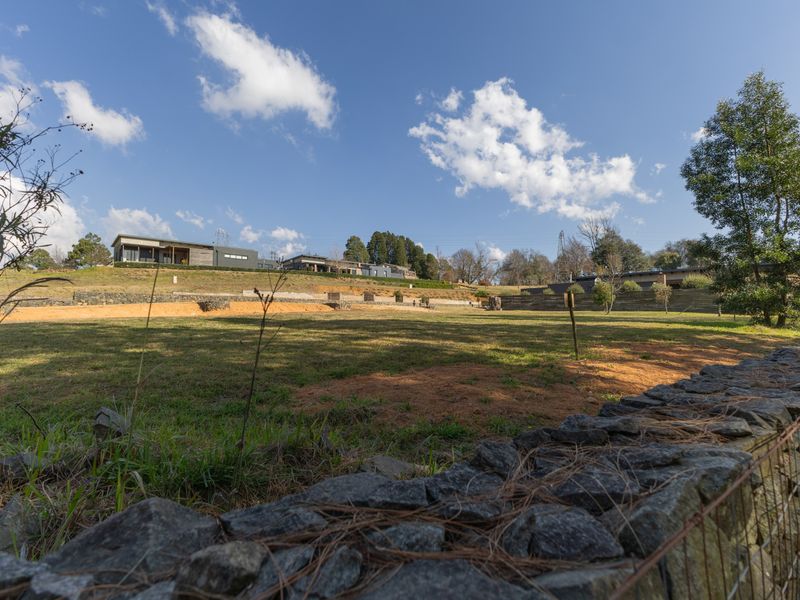 A spacious, well-maintained residential plot featuring a stone retaining wall, wire fencing, and expansive lawn area with surrounding neighborhood views.