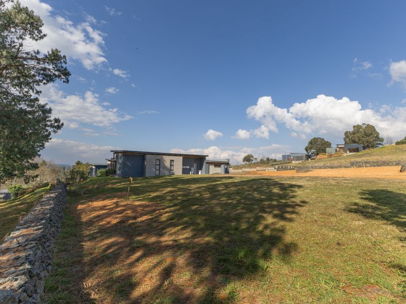 A view of the rear exterior of the property, featuring a stone retaining wall, expansive lawn, and sloped terrain under a clear blue sky.