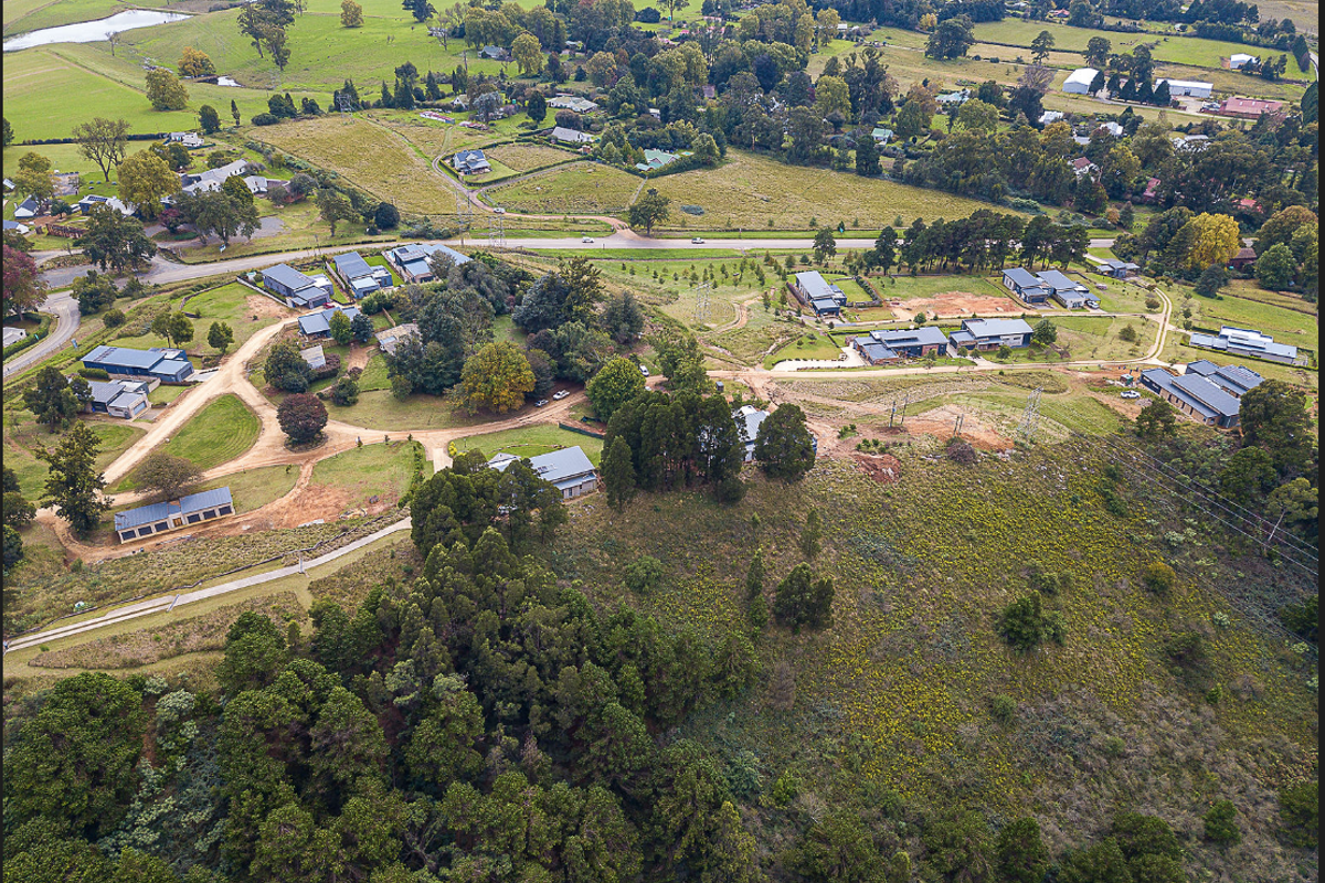 An aerial view of a residential land development showing surrounding infrastructure, established vegetation, and access roads within a rural setting.