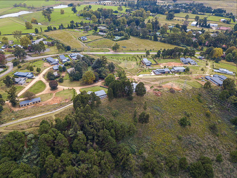 An aerial view of a residential land development showing surrounding infrastructure, established vegetation, and access roads within a rural setting.