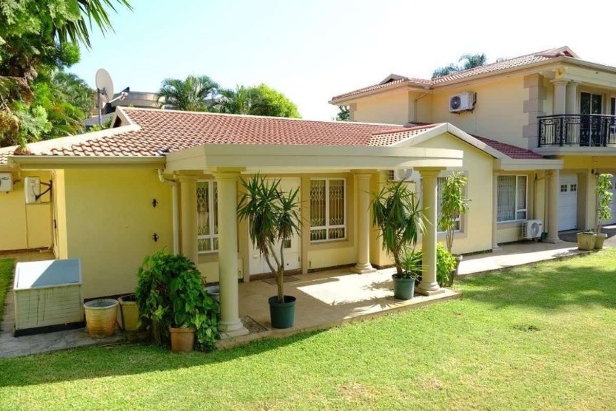 Rear view of a two-story house featuring a covered patio with classical columns, a balcony with wrought iron railings, and a well-maintained lawn.