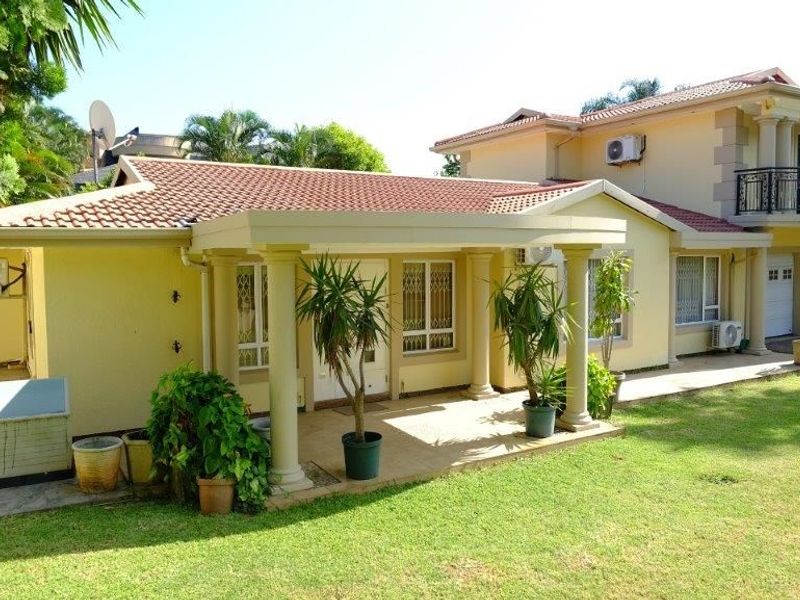 Rear view of a two-story house featuring a covered patio with classical columns, a balcony with wrought iron railings, and a well-maintained lawn.