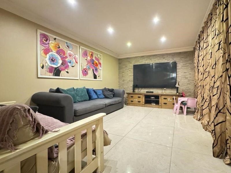 A comfortable living room featuring large format floor tiles, recessed downlighting, and a textured stone feature wall.