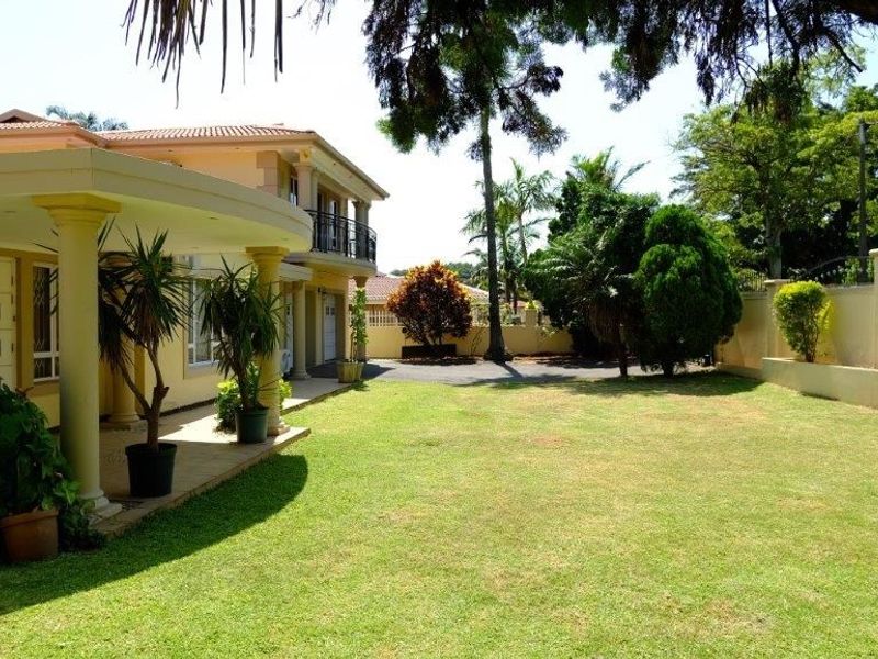A spacious rear garden featuring a covered patio with concrete columns, a well-maintained lawn, and a secure perimeter wall.