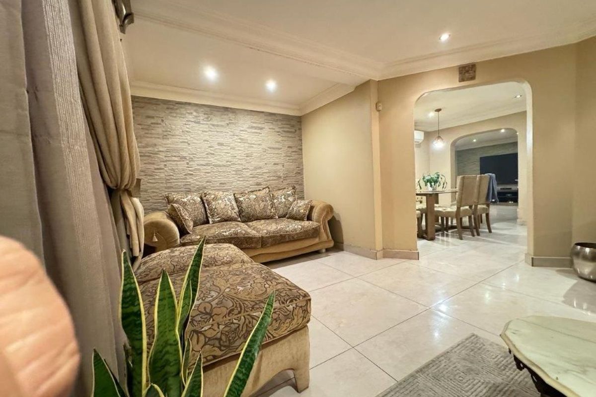 A well-maintained living room featuring a textured stone accent wall, neutral tiled flooring, and an open archway leading to the adjacent dining area.