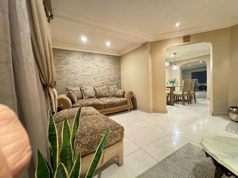 A well-maintained living room featuring a textured stone accent wall, neutral tiled flooring, and an open archway leading to the adjacent dining area.