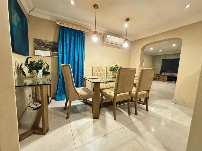 A dining area featuring tiled flooring, recessed lighting, and a split-system air conditioner, leading through an archway into an adjacent living space.