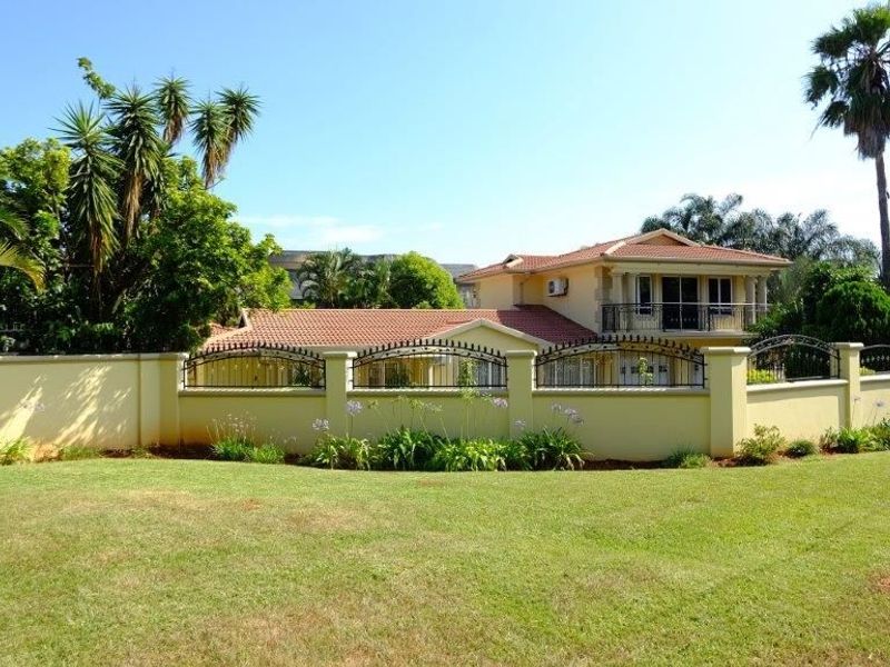 A well-maintained two-story house featuring a tiled roof, a balcony, and a secure perimeter wall with decorative wrought iron fencing.