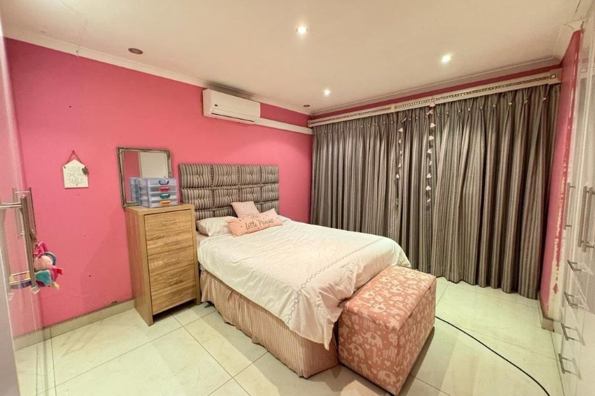 A bedroom featuring tiled flooring, recessed downlighting, a wall-mounted air conditioning unit, and built-in storage cupboards.