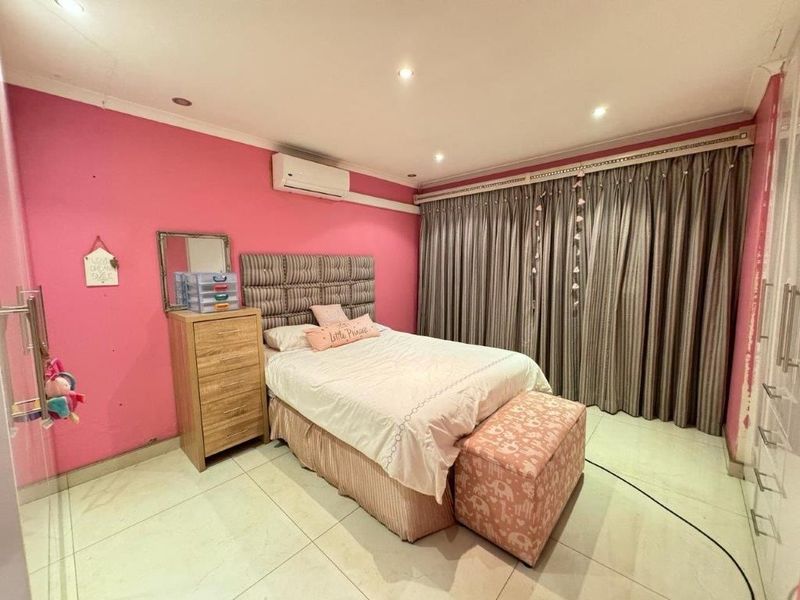 A bedroom featuring tiled flooring, recessed downlighting, a wall-mounted air conditioning unit, and built-in storage cupboards.