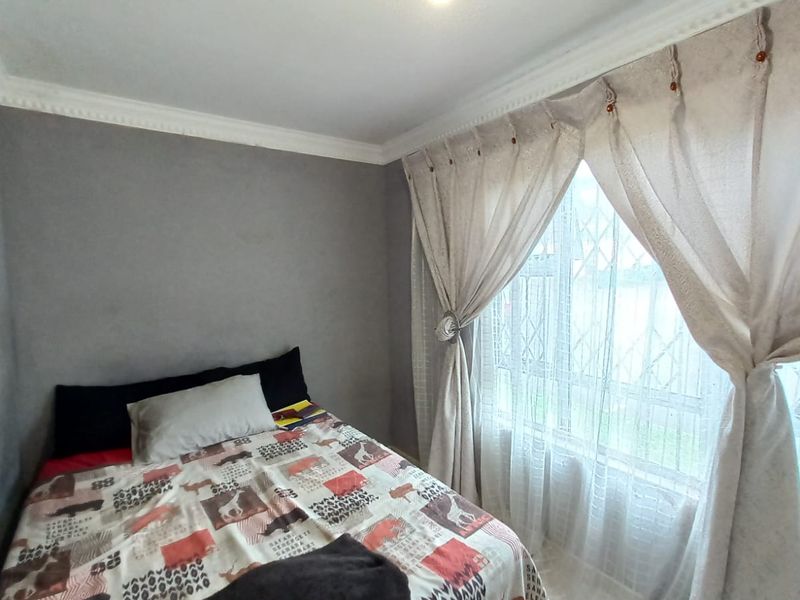 A bedroom featuring neutral grey walls, decorative ceiling cornicing, and a window fitted with a security gate.