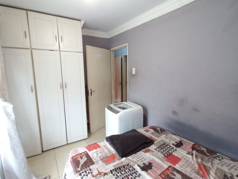 A bedroom featuring built-in cupboards, tiled flooring, and decorative cornice. The walls show visible signs of wear and staining.