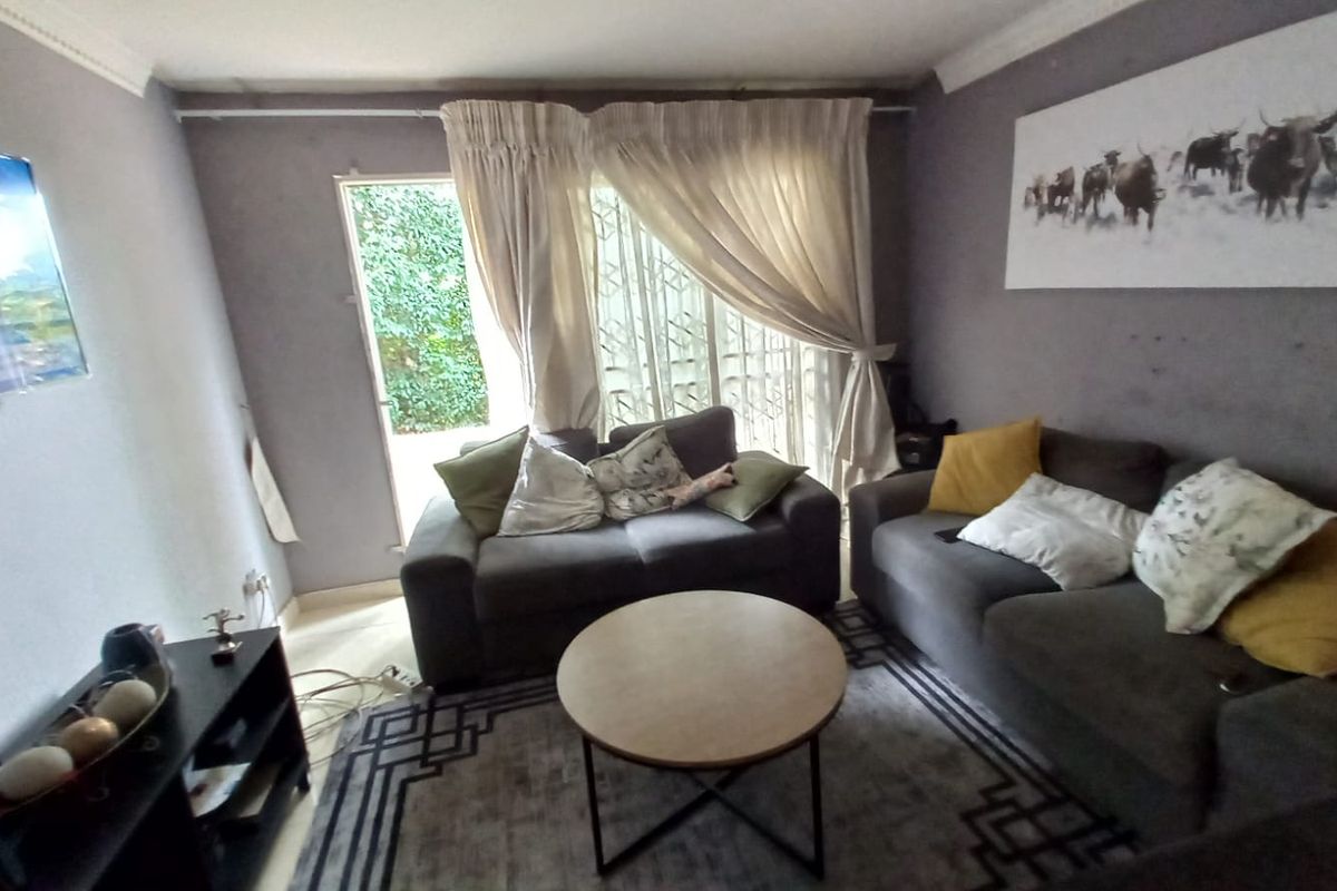 A comfortable living room featuring a sliding glass door with security gate, providing access to the exterior and natural light.