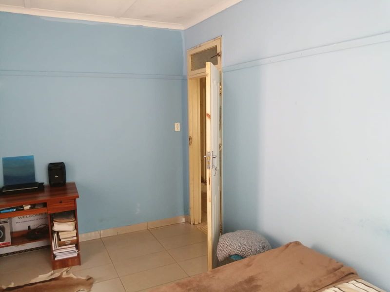A bedroom featuring tiled flooring and light blue walls, currently showing signs of wear and requiring cosmetic updates to improve its overall condition.