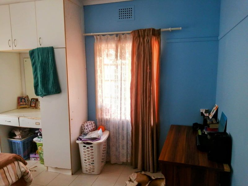 A bedroom featuring blue walls, built-in cupboards with an integrated vanity unit, and a window with curtain tracks.