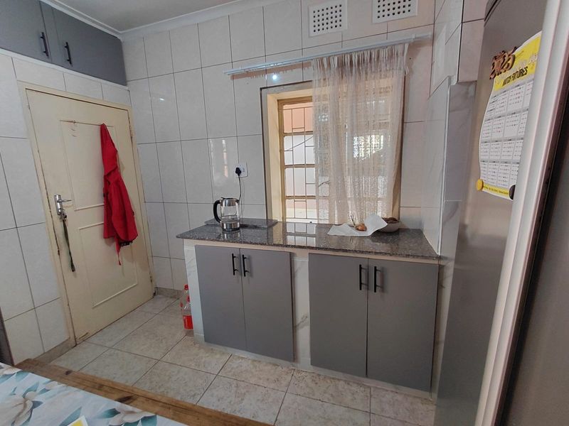 A functional kitchen area featuring modern grey cabinetry, granite countertops, and full-height wall tiling, providing a clean and practical workspace.