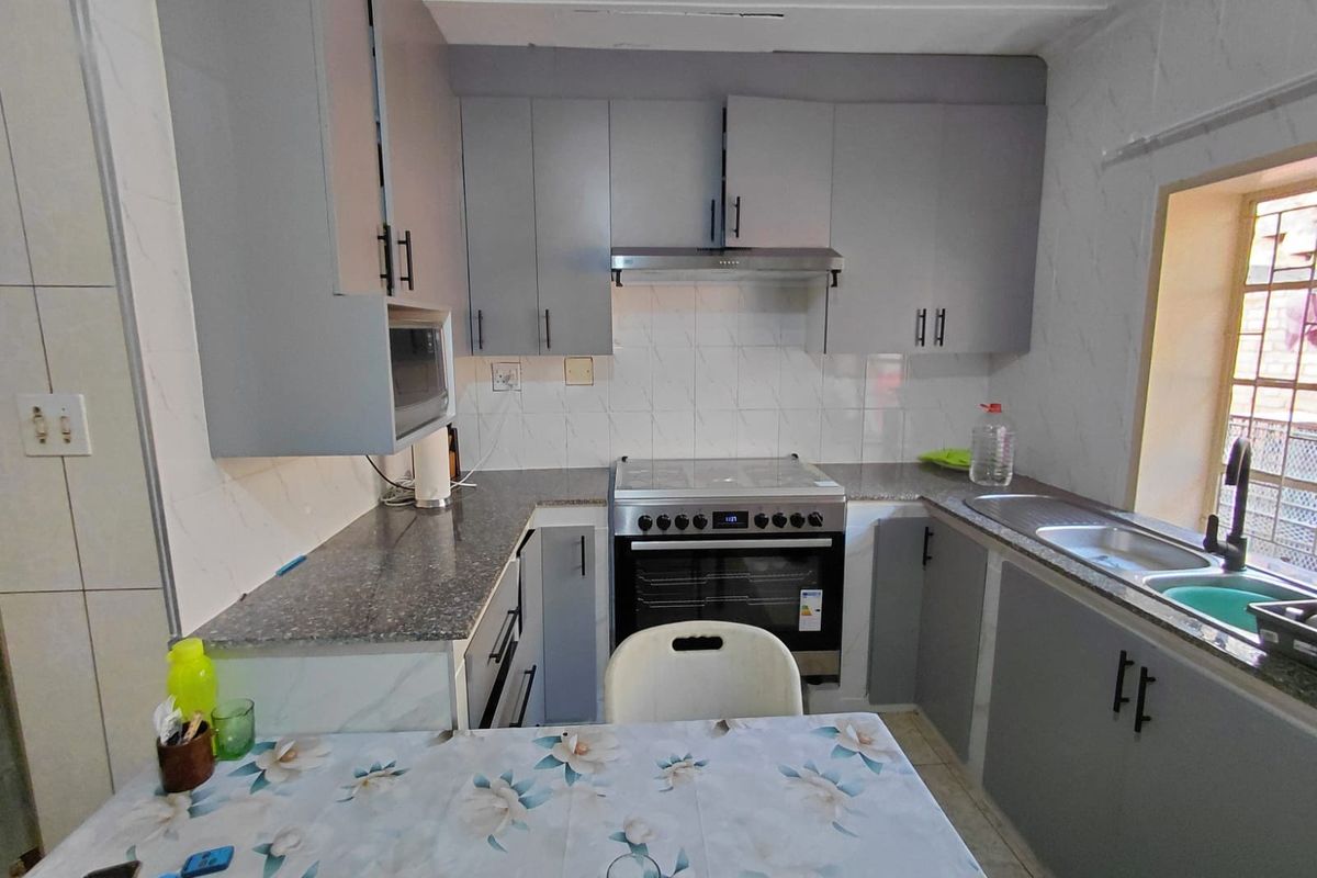 A functional kitchen featuring grey cabinetry, laminate countertops, a stainless steel sink, and a freestanding stove with an extractor fan.