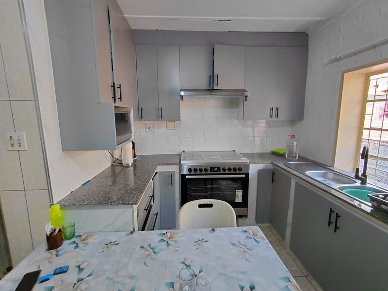 A functional kitchen featuring grey cabinetry, laminate countertops, a stainless steel sink, and a freestanding stove with an extractor fan.