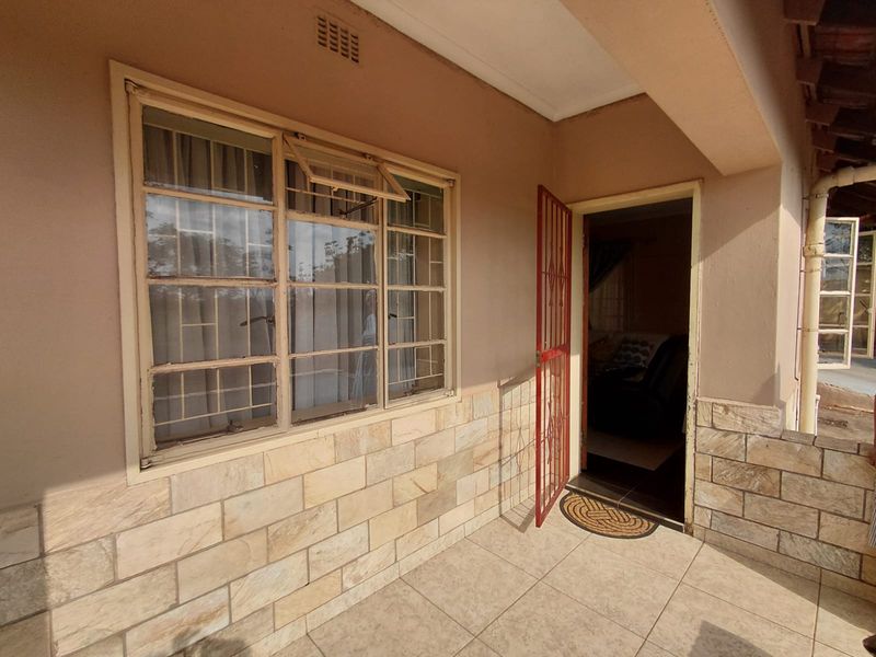 A covered patio area featuring tiled flooring, stone cladding accents, and a secure entrance door with steel window frames.