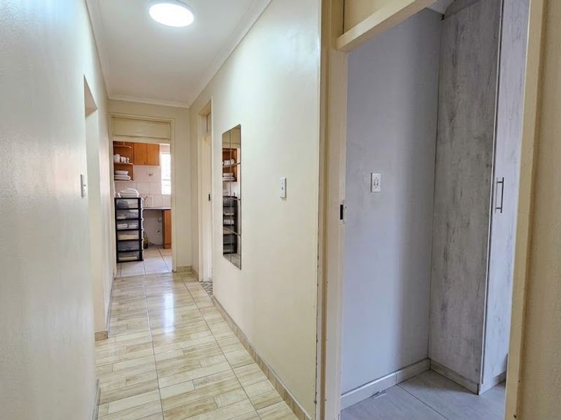 A clean, functional hallway featuring tiled flooring, neutral wall finishes, and a built-in cupboard, providing access to adjacent rooms.
