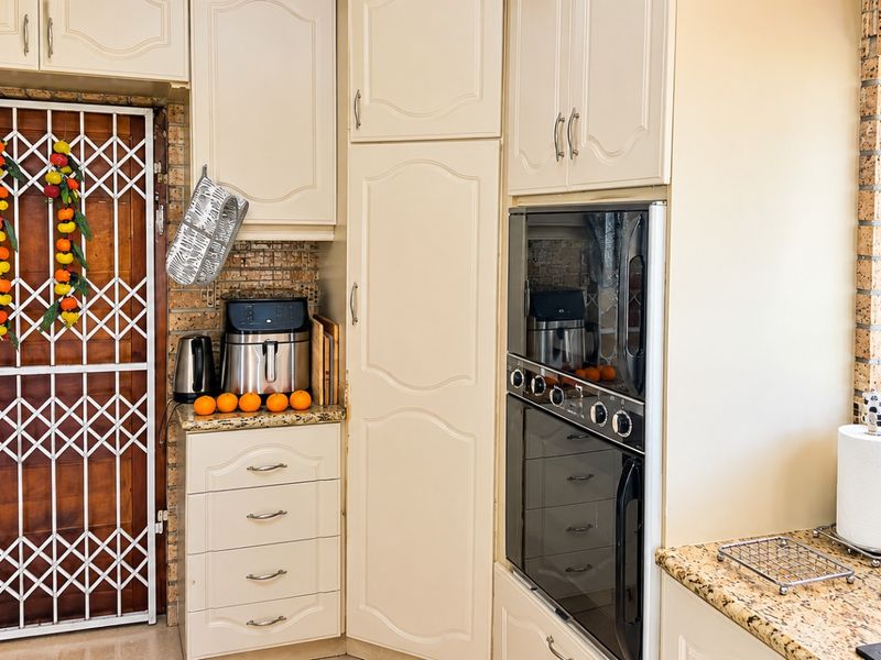 A functional kitchen featuring cream-colored cabinetry, granite countertops, a built-in oven, and a brick feature wall with a security gate.