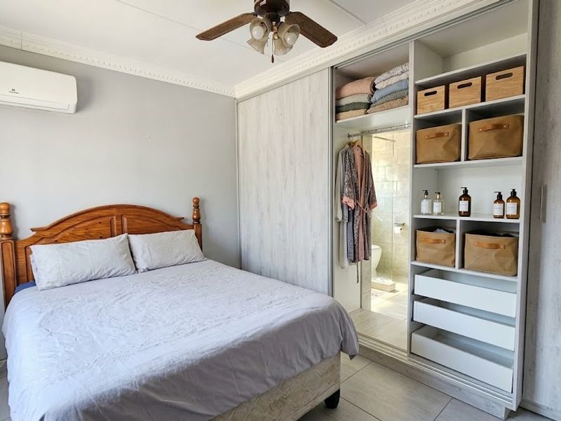A well-maintained bedroom featuring a built-in wardrobe with open shelving, a ceiling fan, and a wall-mounted air conditioning unit.