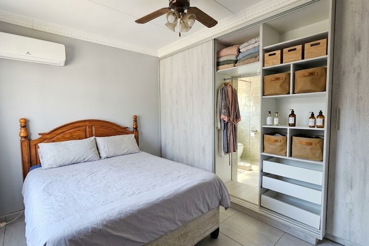 A well-maintained bedroom featuring a built-in wardrobe with open shelving, a ceiling fan, and a wall-mounted air conditioning unit.