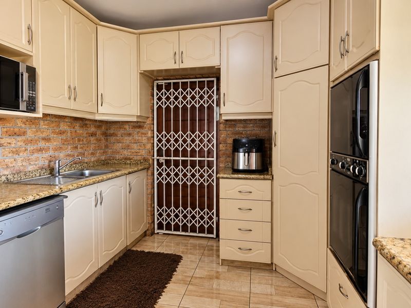 A functional kitchen featuring cream cabinetry, granite countertops, a brick splashback, and integrated appliances including an oven and microwave.