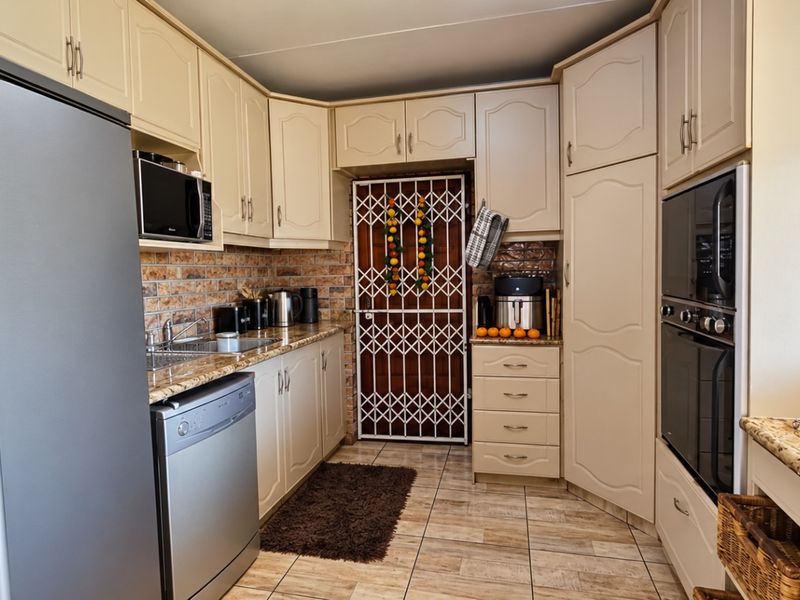 A functional kitchen featuring cream-colored cabinetry, granite countertops, a brick backsplash, and integrated appliances including a double oven and microwave.