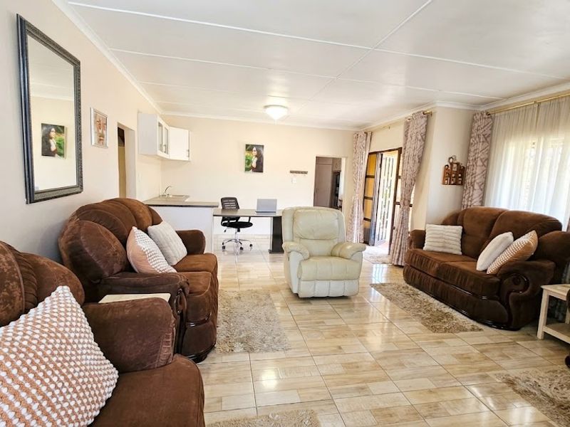 Spacious open-plan living area featuring tiled flooring, integrated kitchen cabinetry with sink, and access to an outdoor patio through a sliding door.