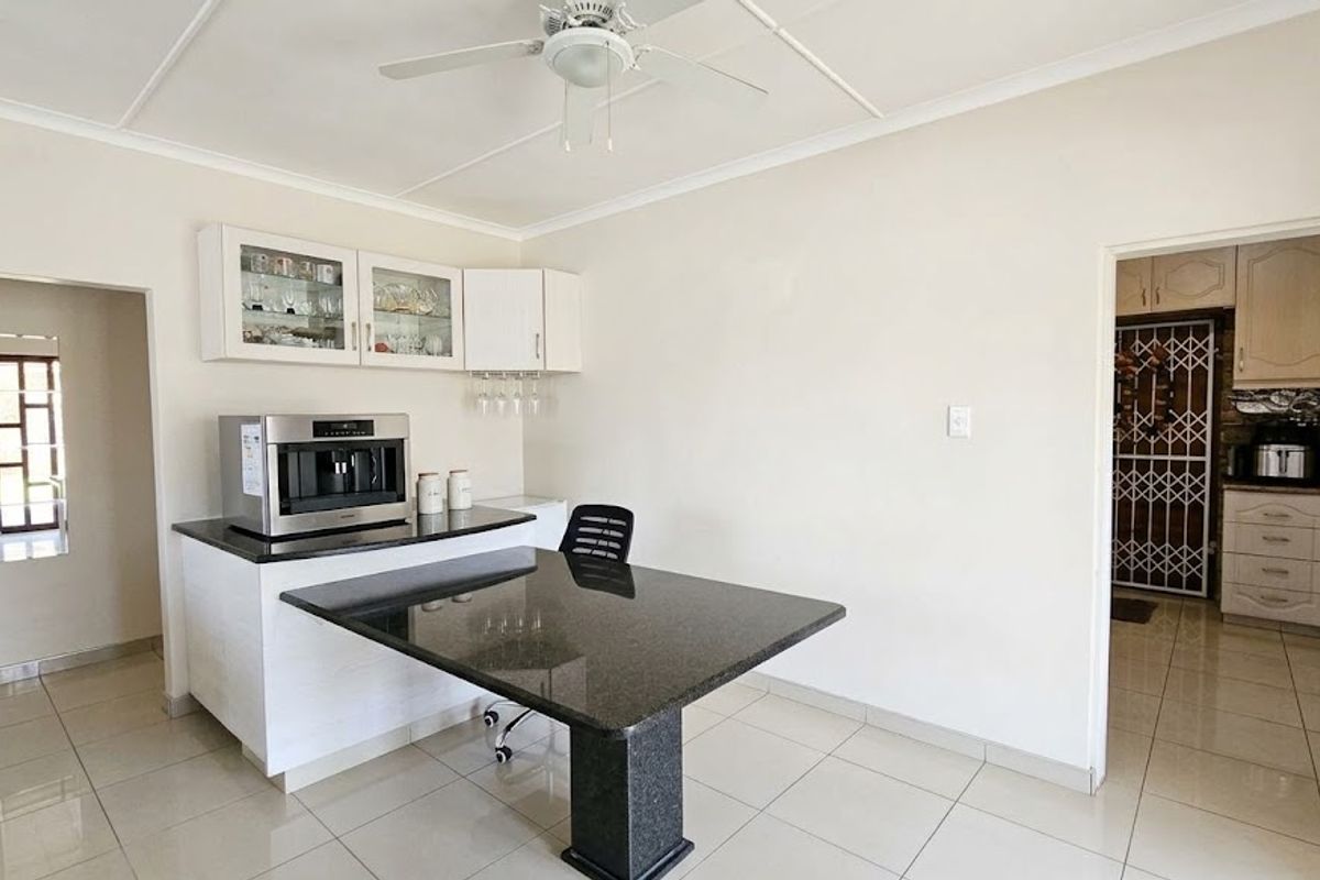 A functional kitchen area featuring granite countertops, built-in cabinetry with glass-front displays, and tiled flooring, with an adjacent scullery visible through the doorway.