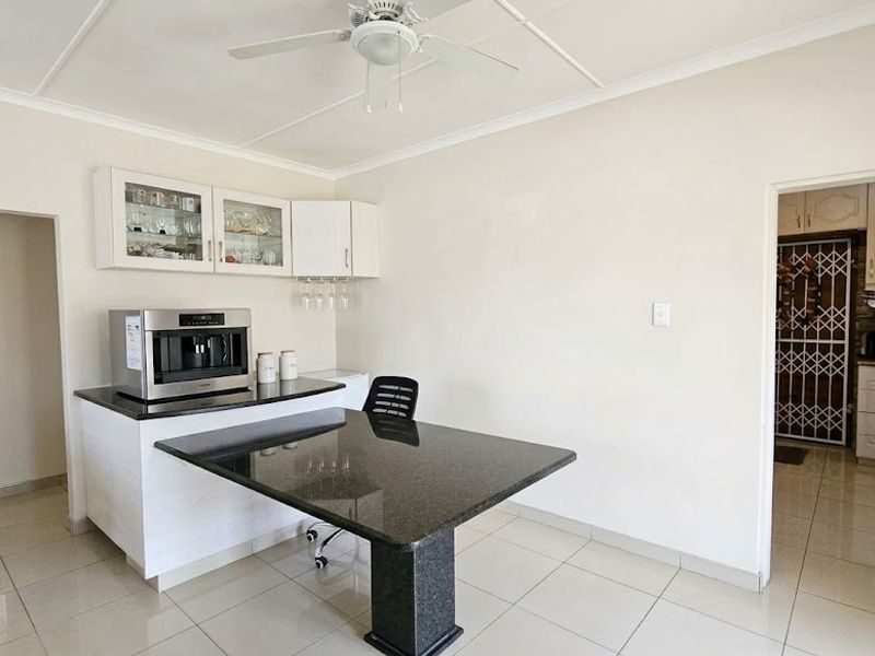 A functional kitchen area featuring granite countertops, built-in cabinetry with glass-front displays, and tiled flooring, with an adjacent scullery visible through the doorway.