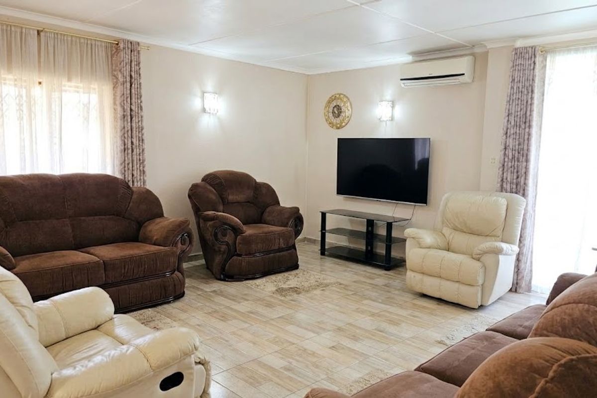 A comfortable living room featuring tiled flooring, wall-mounted air conditioning, and dual wall sconces, providing a functional and well-lit space.