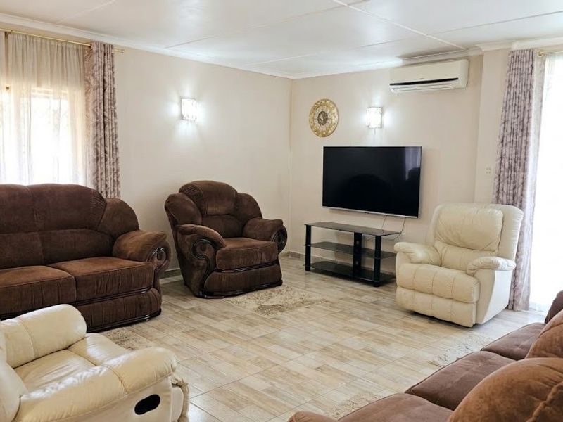 A comfortable living room featuring tiled flooring, wall-mounted air conditioning, and dual wall sconces, providing a functional and well-lit space.