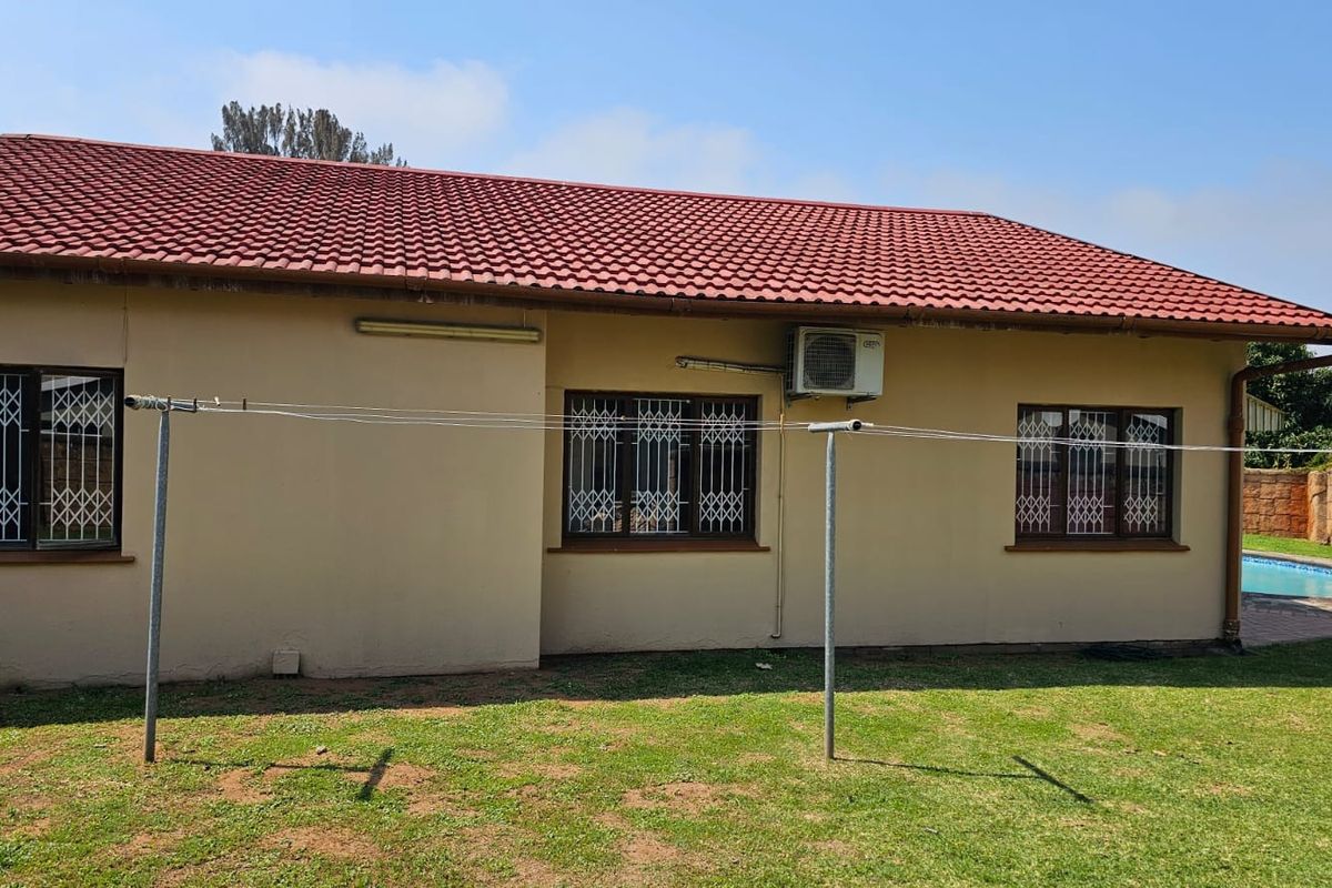 Rear elevation of the house featuring a tiled roof, security bars on windows, and an external air conditioning unit overlooking the garden.