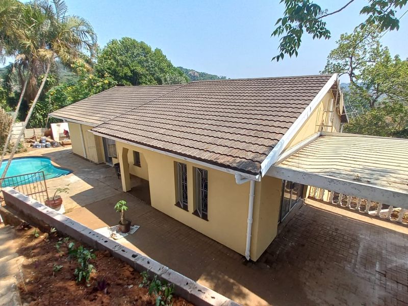 Rear view of the house featuring a swimming pool, paved patio area, and a covered carport structure set within a landscaped garden.
