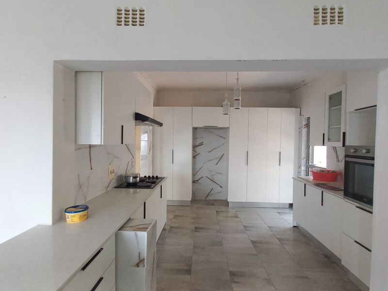A modern, spacious kitchen featuring white cabinetry, stone countertops, built-in oven, gas hob, and tiled flooring with a clean, minimalist aesthetic.