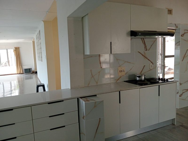 Modern kitchen featuring sleek white cabinetry, stone countertops, a built-in hob with extractor fan, and a convenient breakfast bar overlooking the living area.