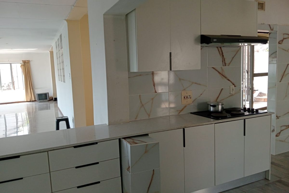 Modern kitchen featuring sleek white cabinetry, stone countertops, a built-in hob with extractor fan, and a convenient breakfast bar overlooking the living area.