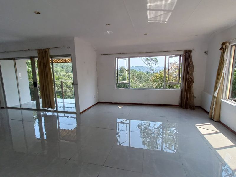Spacious, light-filled living area featuring large windows, sliding glass doors leading to a balcony, and polished tiled flooring with scenic views.