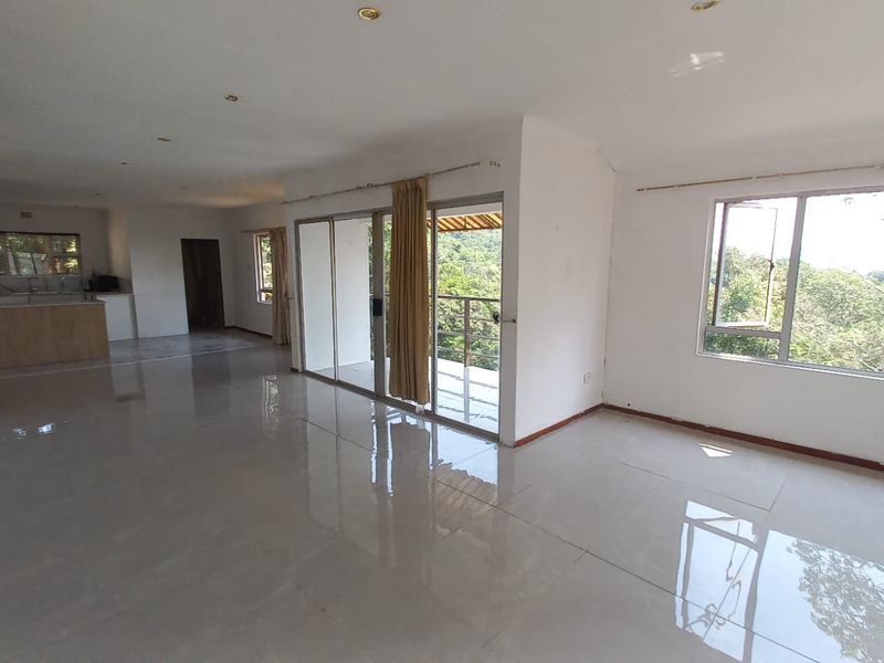 Spacious open-plan living area featuring large windows, tiled floors, and direct access to an outdoor balcony with scenic views.