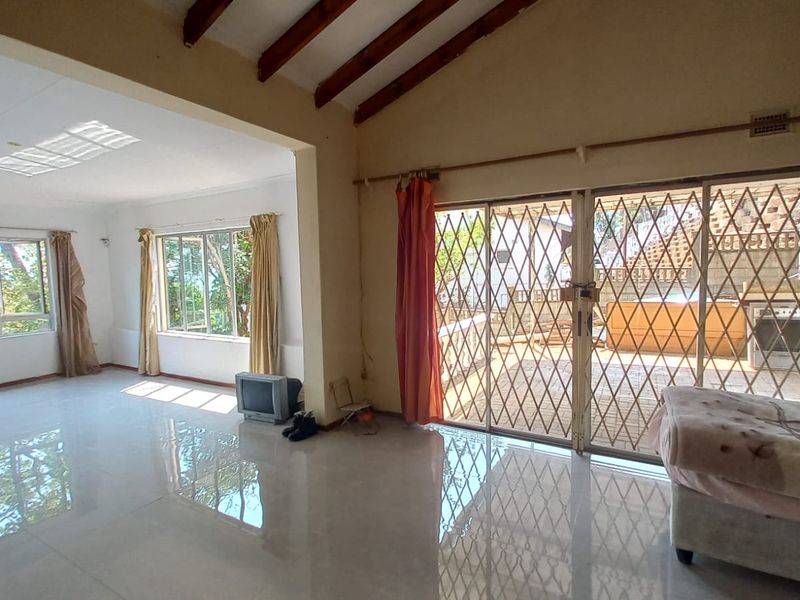 Spacious living area featuring exposed timber ceiling beams, large windows for natural light, and sliding glass doors leading to an outdoor patio.