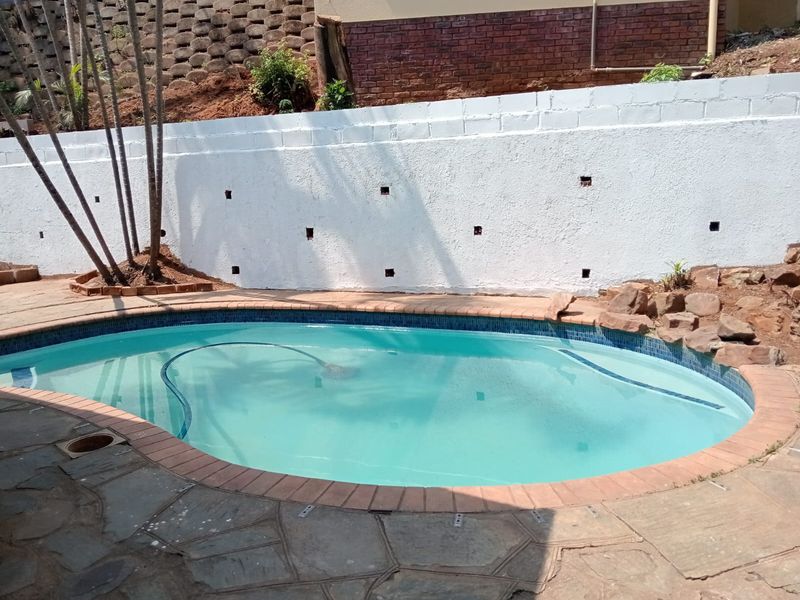 Outdoor swimming pool area featuring stone paving, brick coping, and a white painted retaining wall backdrop.