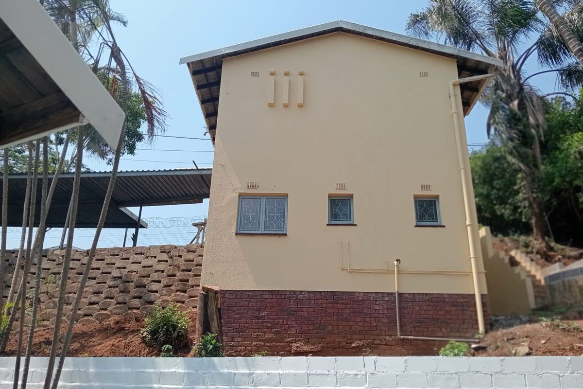 Rear elevation of the property featuring a brick plinth, plastered walls, security-fitted windows, and a concrete block boundary wall with a retaining wall structure.