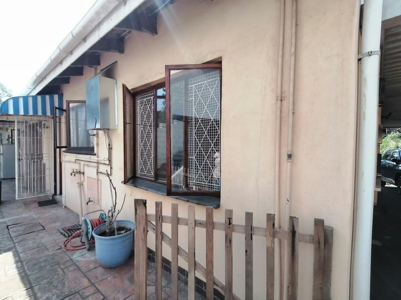 Rear exterior view of the cottage featuring a tiled patio area, gas geyser installation, and security-fitted windows with a timber fence.