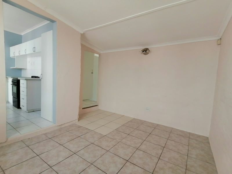 An empty open-plan living area featuring tiled floors and coved ceilings, with an adjacent kitchen space containing built-in cabinetry and a stove.