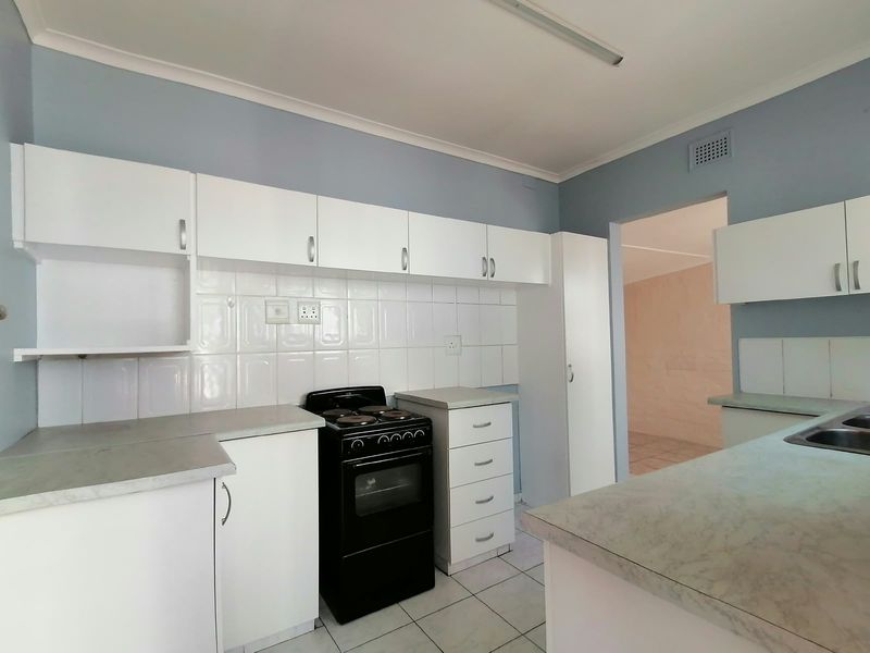 A functional kitchen featuring white cabinetry, tiled backsplash, laminate countertops, and a freestanding electric stove, offering a clean and practical workspace.