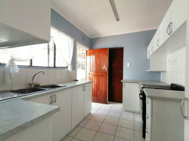 A functional kitchen featuring white cabinetry, laminate countertops, a double bowl sink, and ceramic floor tiles, providing a clean and practical workspace.
