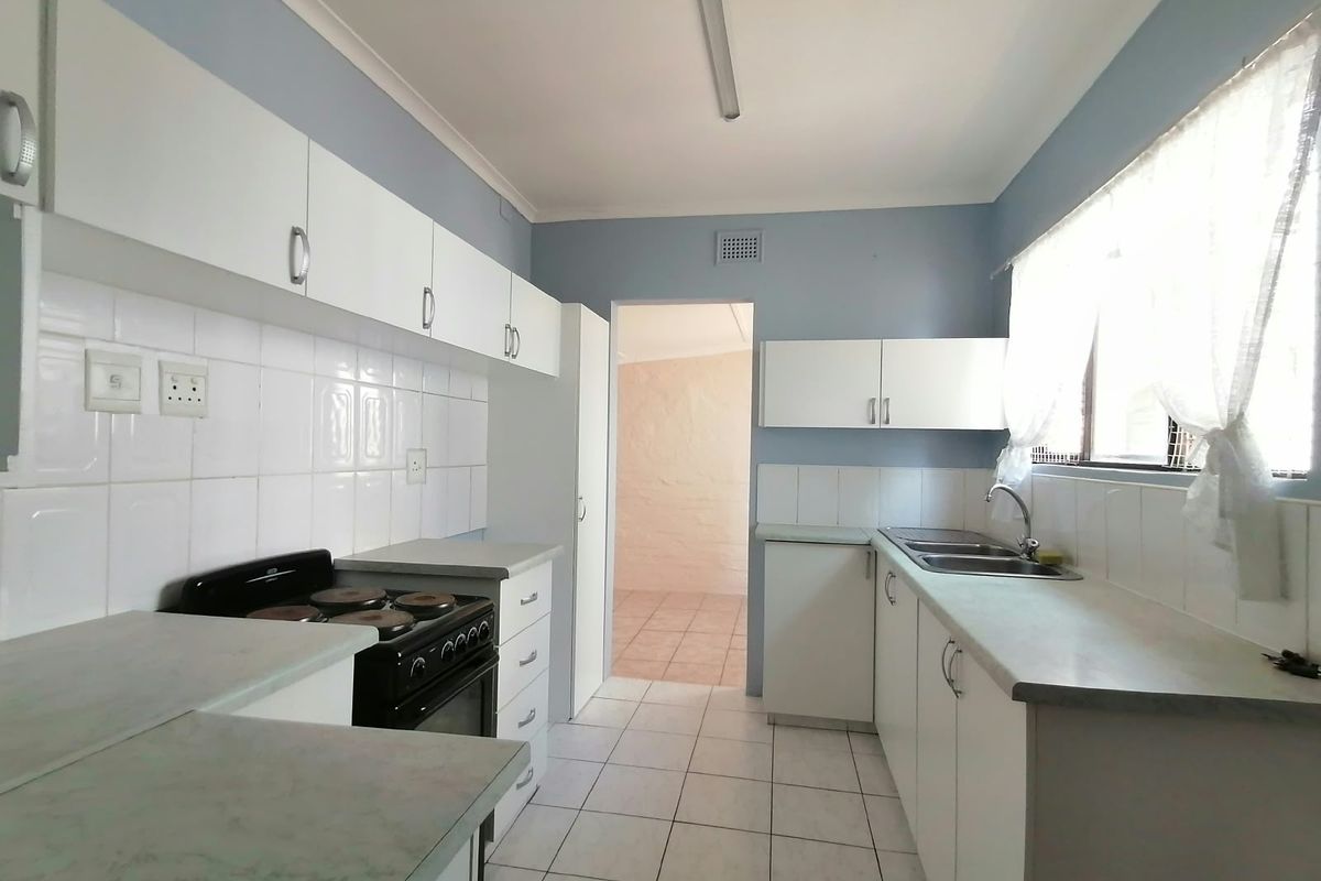 Functional kitchen featuring white cabinetry, laminate countertops, tiled splashbacks, and a freestanding stove, offering a clean and practical workspace.