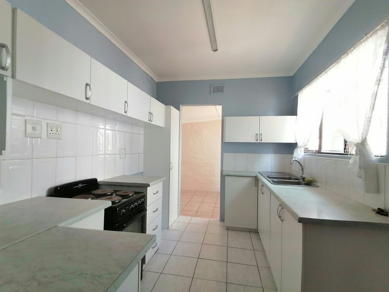 Functional kitchen featuring white cabinetry, laminate countertops, tiled splashbacks, and a freestanding stove, offering a clean and practical workspace.
